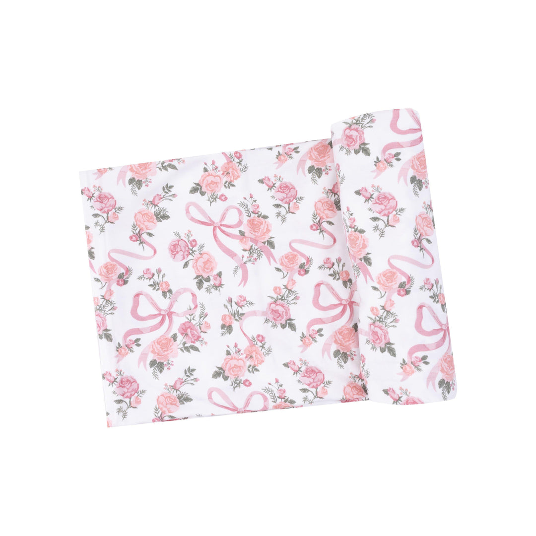 white baby swaddle with pink roses and tiny ribbons makeing a bow printed on the swaddle