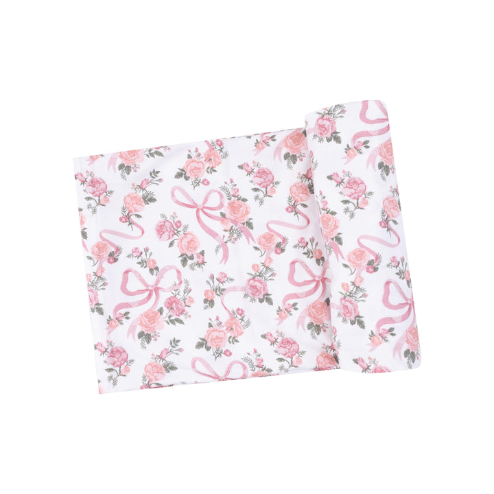 white baby swaddle with pink roses and tiny ribbons makeing a bow printed on the swaddle