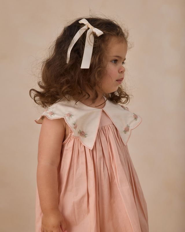 Young girl wearing a pink dress with a white collar against a beige background