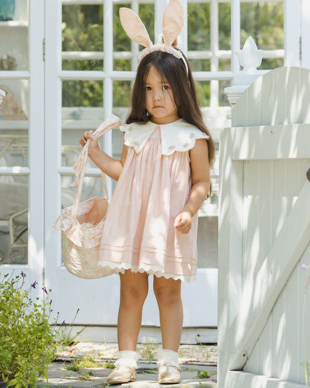 Young girl in a pink dress with bunny ears standing outdoors.