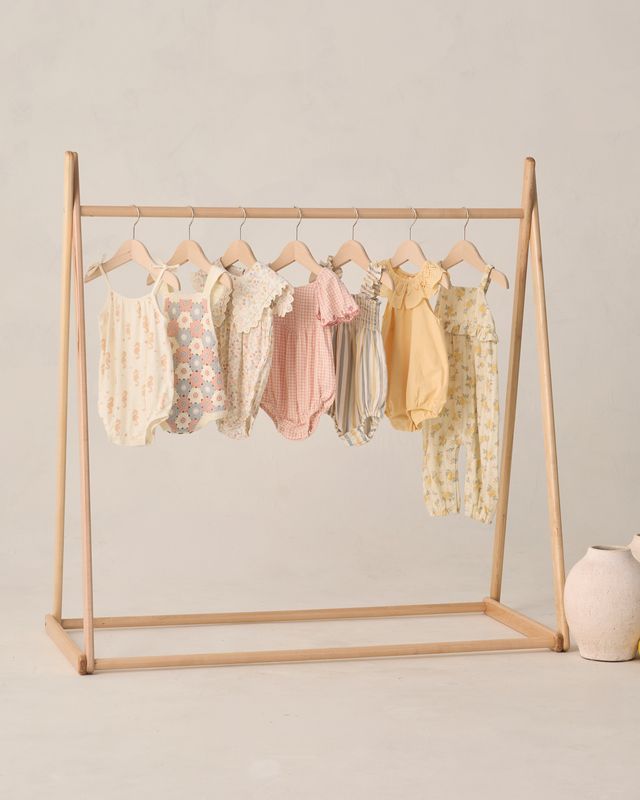 Wooden clothing rack with baby rompers on a plain background