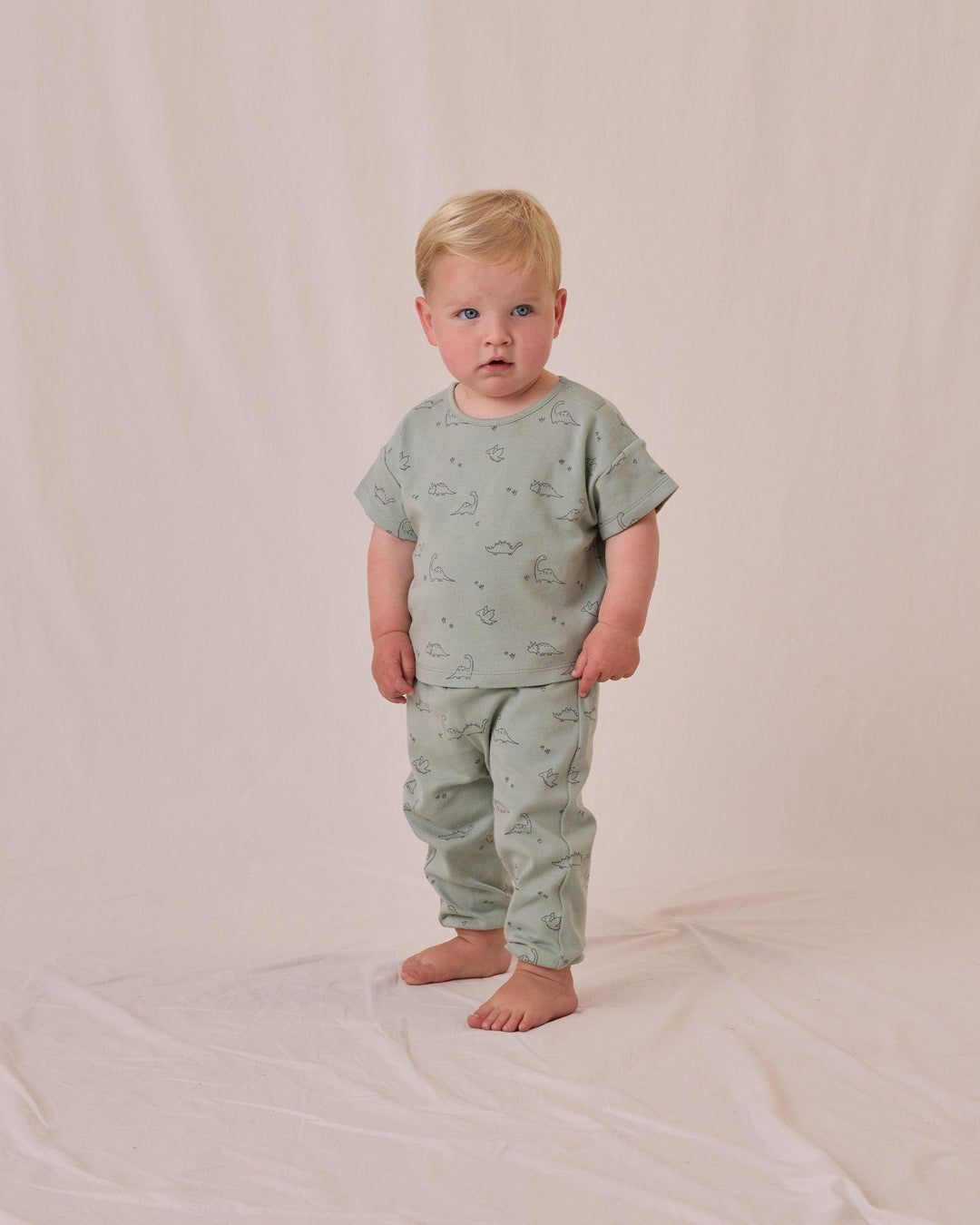 little boy wearing the dino lounge set, sage green colorway- short sleeve tee and pants. tiny dino printed all over. 