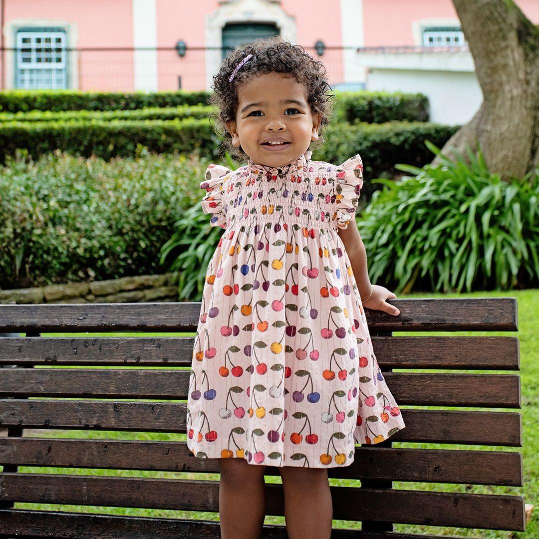 young girl modeling the stevie style dress with cherries printed all over it.  This picture shows the dress hits the small child at the knee