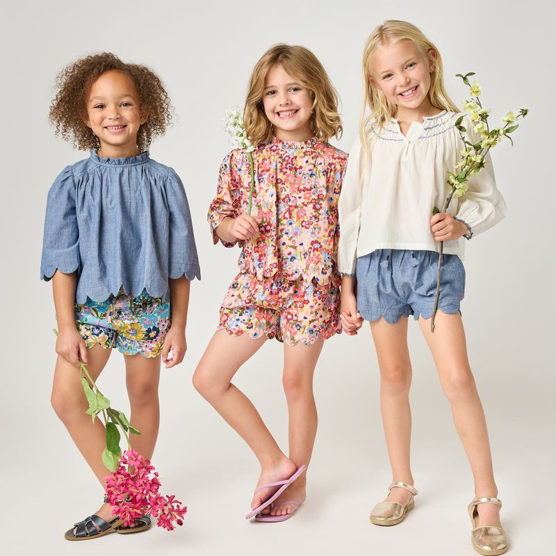 Three young girls wearing colorful outfits with flowers and plants on a plain background