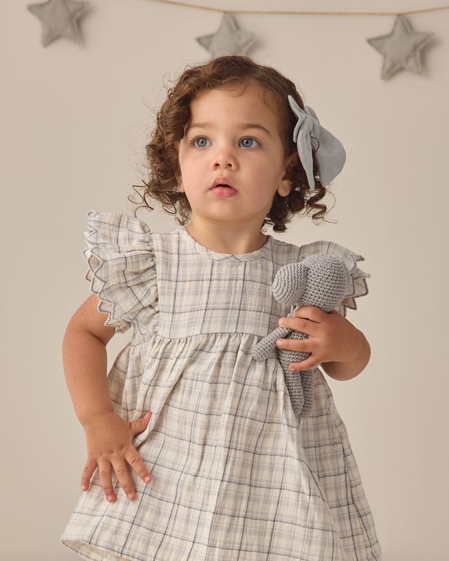 Child wearing a plaid dress holding a toy with star decorations on the wall.
