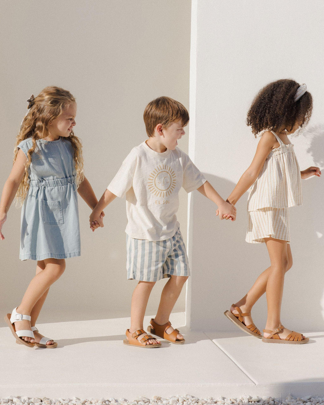 3 kids walking holding hands one of the little boys is wearing the ocean stripe shorts. 