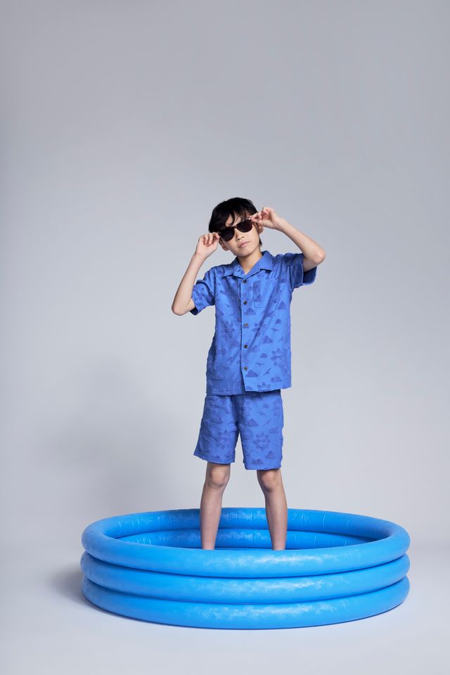 Child in a blue outfit standing next to a small blue inflatable pool on a plain background