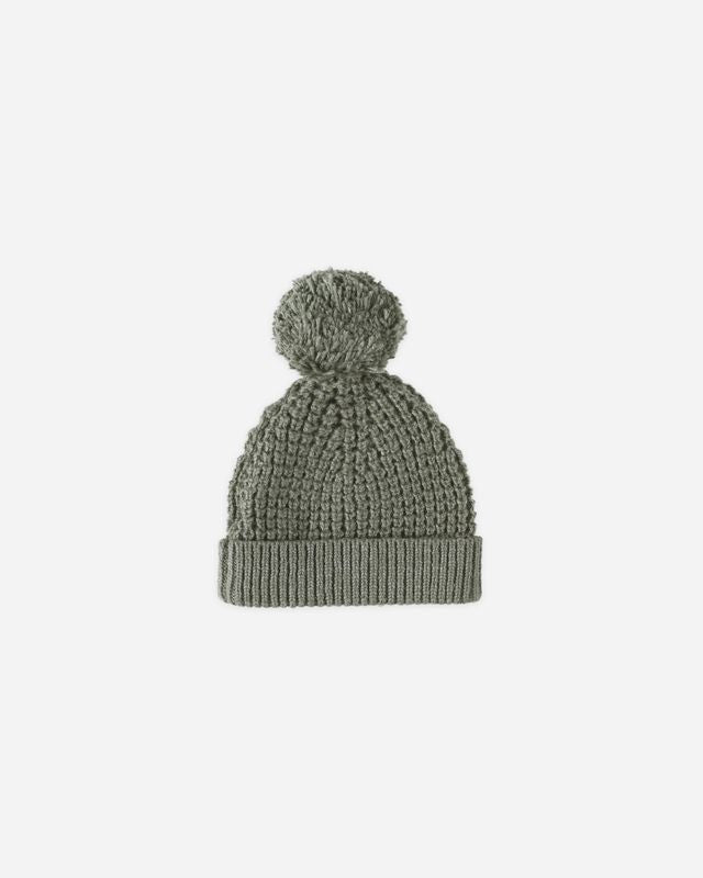 Green knit beanie with pom-pom on a light gray background