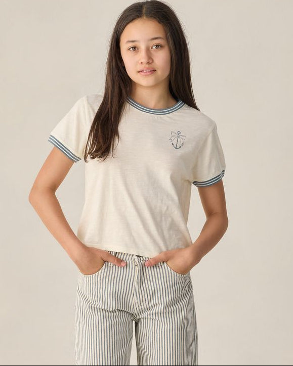 Person wearing a white t-shirt with an anchor design on a plain background