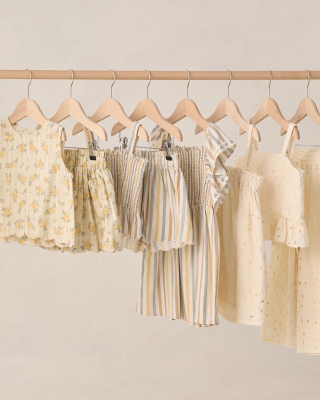 Row of children's dresses on wooden hangers against a plain background
