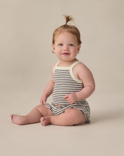 Baby sitting on a beige surface with white clouds in the background