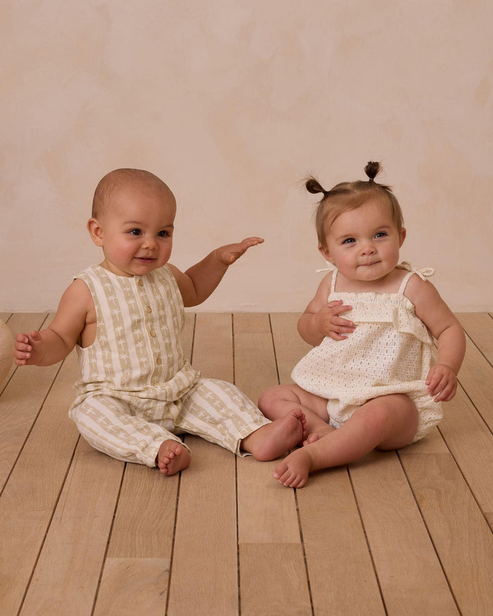 two babies sitting in rylee and cru outfits. one in palm stripe jumpsuit and the other in an ivory eyelet bubble. 