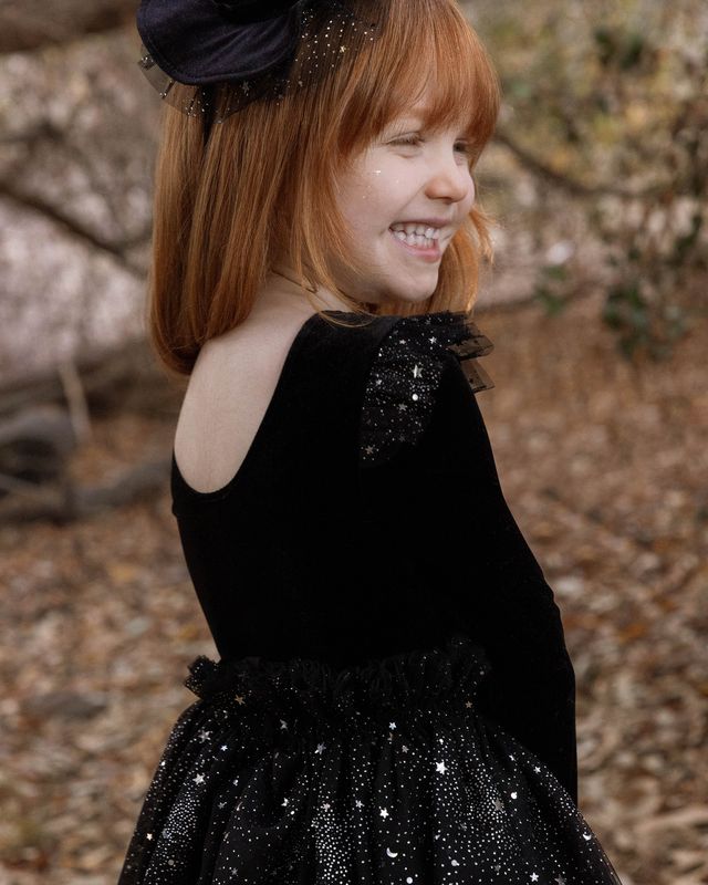 Young girl wearing a black dress with sequin details outdoors.
