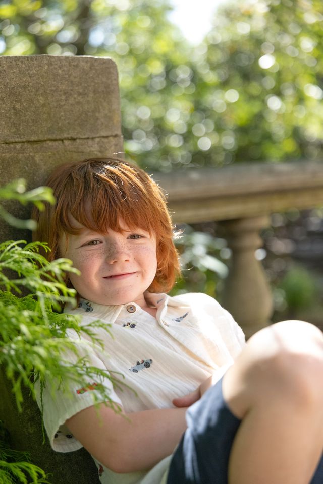 Child with red hair sitting outdoors near greenery