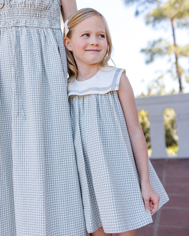 child wearing matching green checkered dresses outdoors.
