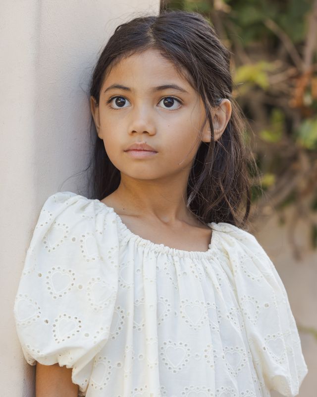 Young girl wearing a white dress with puffed sleeves against a neutral background
