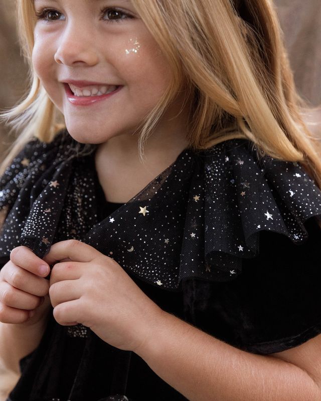 Young girl wearing a black dress with star patterns, smiling.