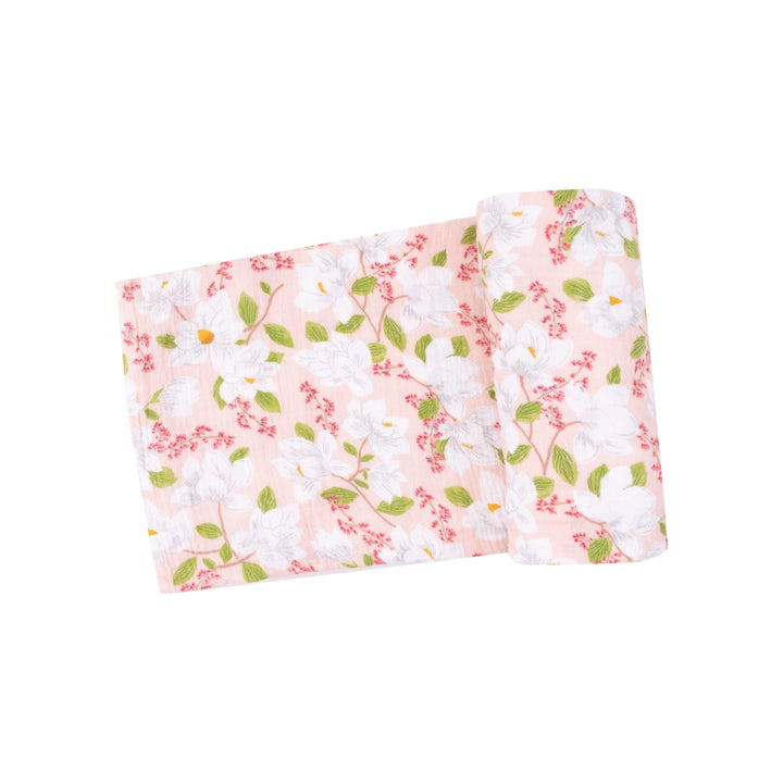 pink swaddle with white magnolias printed on the swaddle. tiny dark pink flowers are also on the swaddle near the magnolias