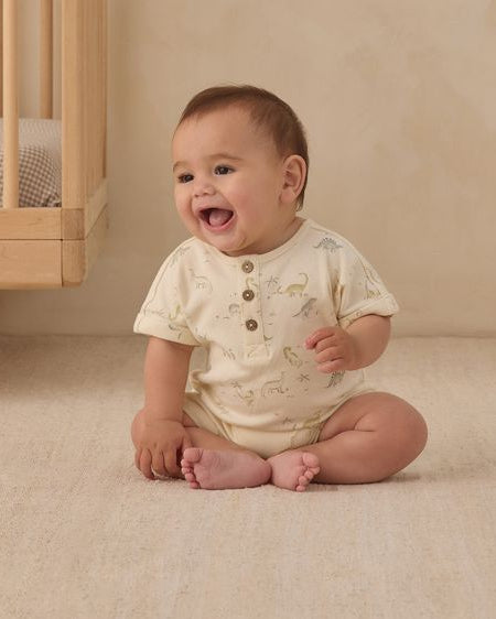 Baby sitting on a beige floor next to a wooden crib.