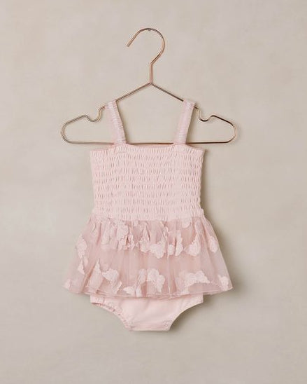 Pink baby romper with butterfly pattern on a beige hanger against a beige background