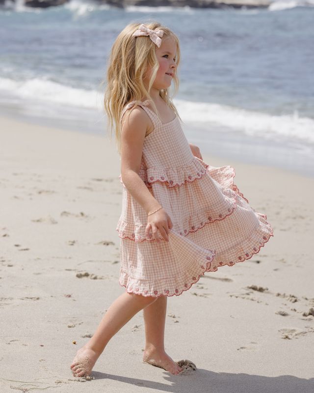 Young girl in a pink dress walking on a sandy beach with ocean waves in the background