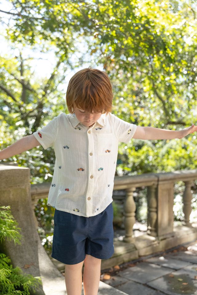 Child standing outdoors with arms outstretched, surrounded by greenery