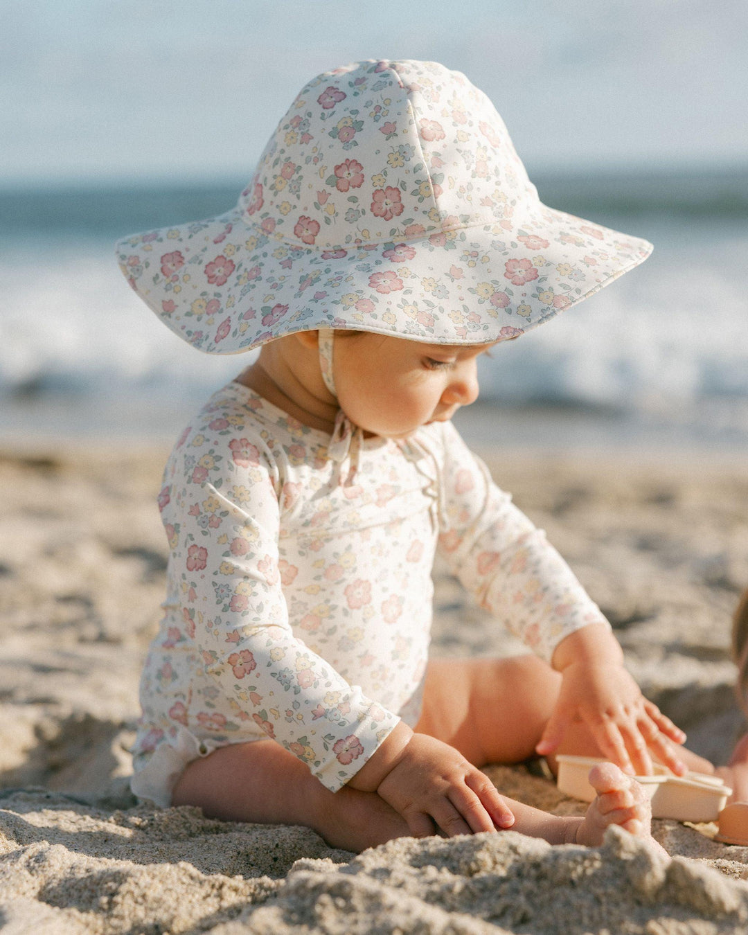 baby girl modeling the rashguard bathing suit in the bloom print. and the hat in the same print as well. tiny pastel floral print. 