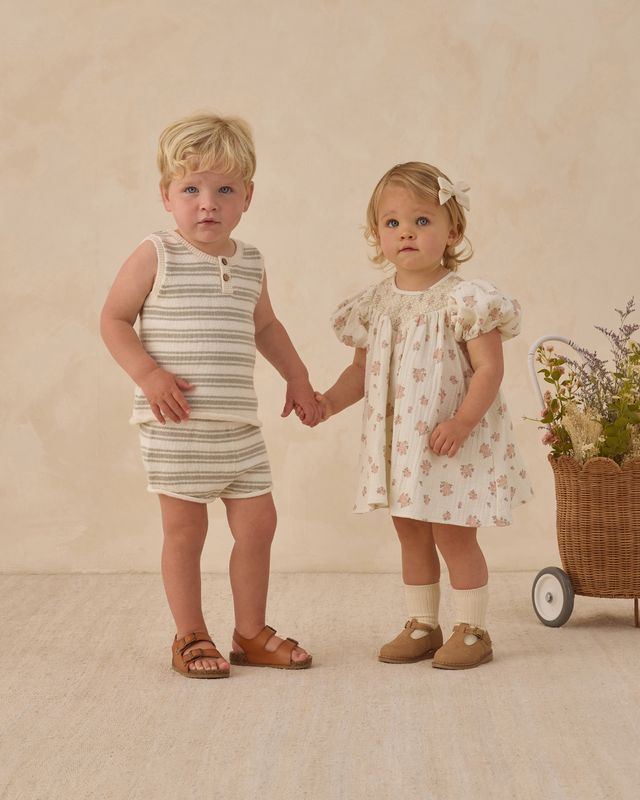 Two children holding hands in front of a beige background with a basket of flowers.