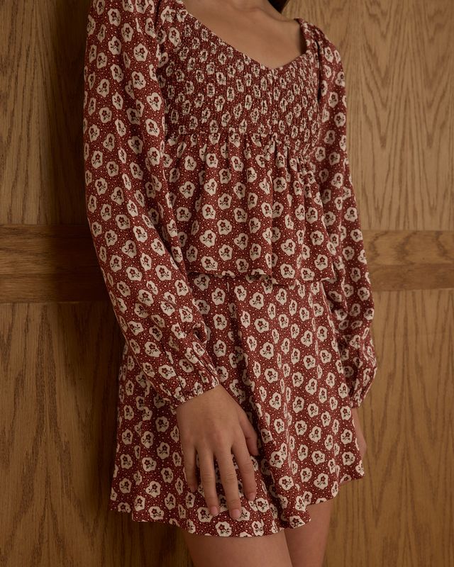 Red floral dress worn by a young girl leaning against a wooden panel background