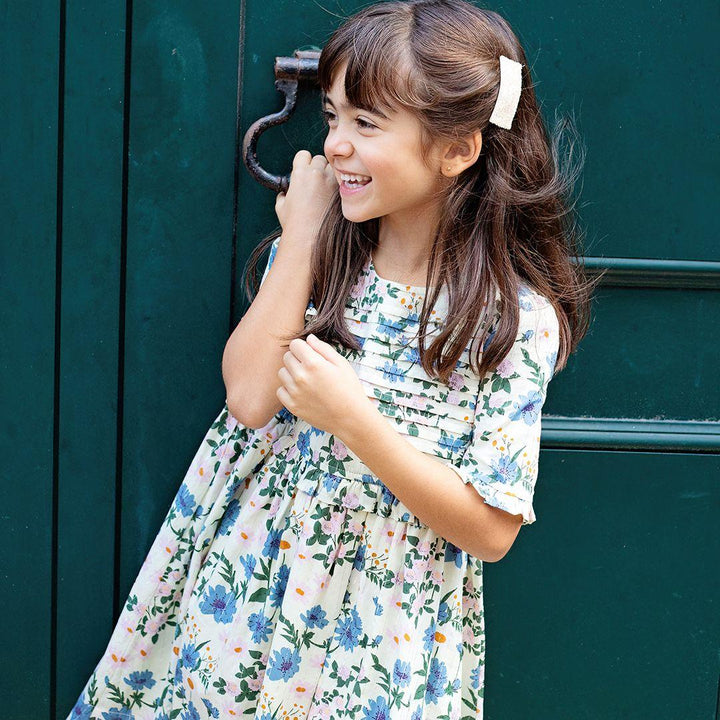 young girl modeling the ivory dress with blue and lavender flowers with pops of orange. the girl is laughing and the wind is blowing. 