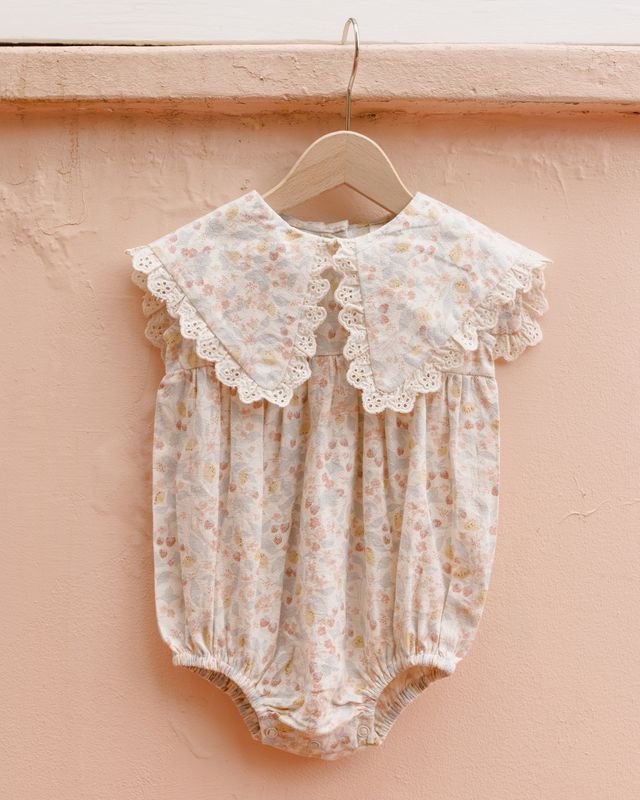 Baby romper with lace details on a hanger against a pink background