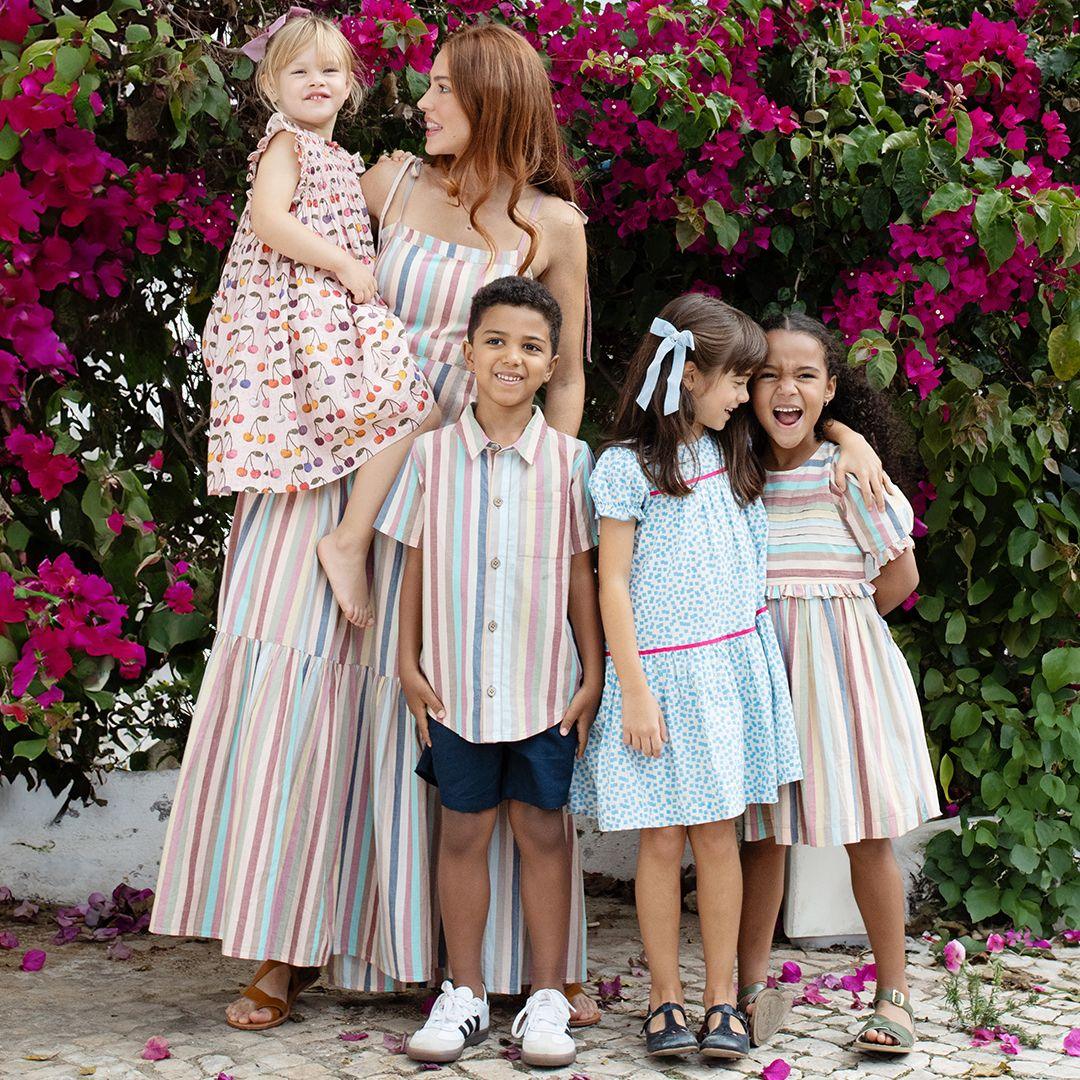This picture shows a few kids and an adult woman all standing together dressed up in coordinating looks. the boy in the front is wearing the navy chinos and multi pastel stripe collared shirt. 
