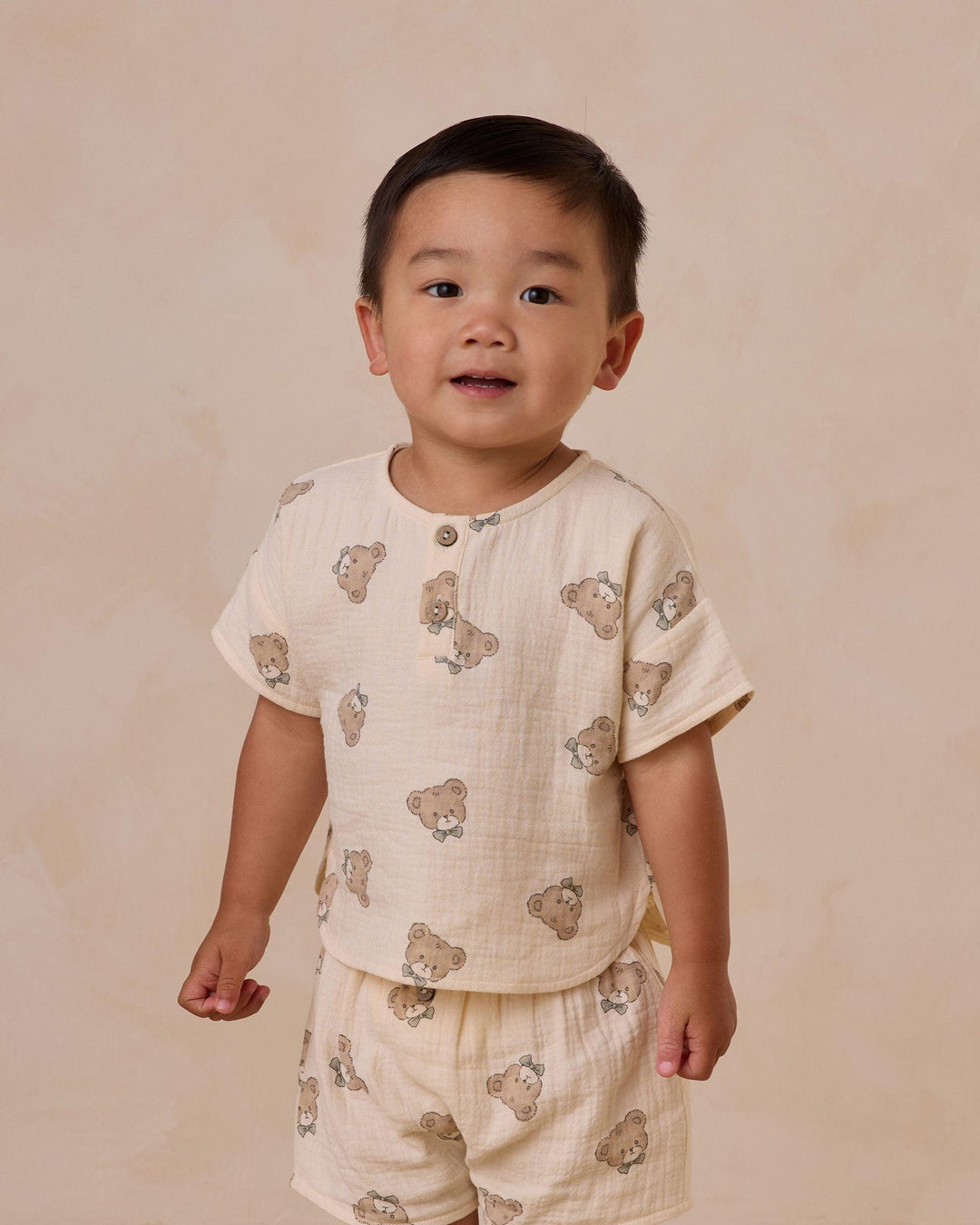 little boy wearing two piece set, beige color with little teddy bear faces on it. 