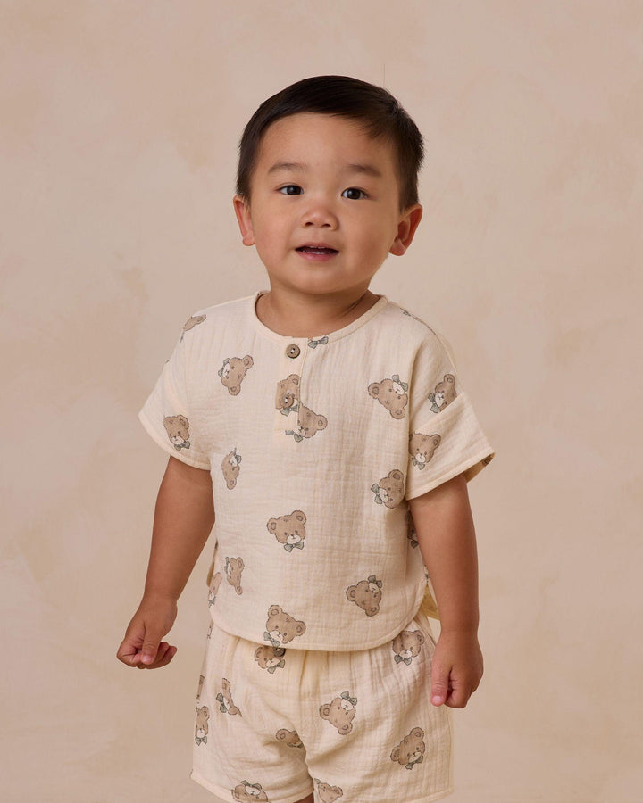 little boy wearing two piece set, beige color with little teddy bear faces on it. 
