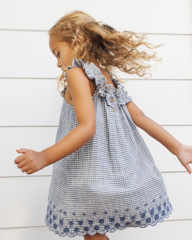 Young girl in a blue checkered dress with floral details against a white background
