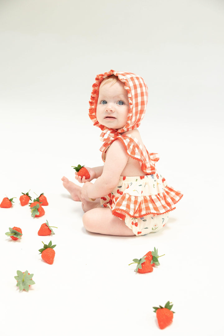 baby modeling the ruffle sunsuit with cherries and sitting from the side. at this angle you can see how the ruffles in the back add such a wonderful detail. 