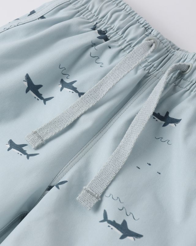 Light blue swim shorts with shark pattern on a light gray background
