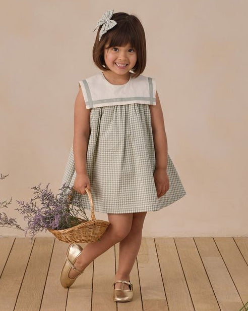 Young girl in a checkered dress holding a basket of flowers on a wooden floor.