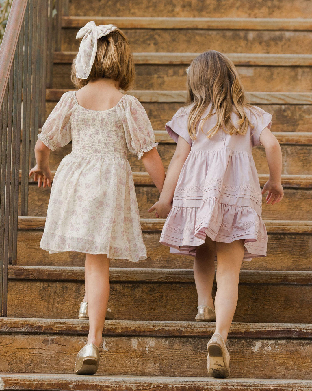 two little girls going up the steps wearing the millie dress and another a lavender dress. the back of the millie smocked and hits righ above the knee