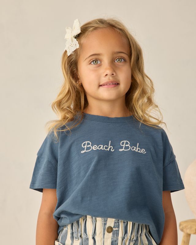 young girl wearing a navy tee that says 'Beach Babe' across the front 
