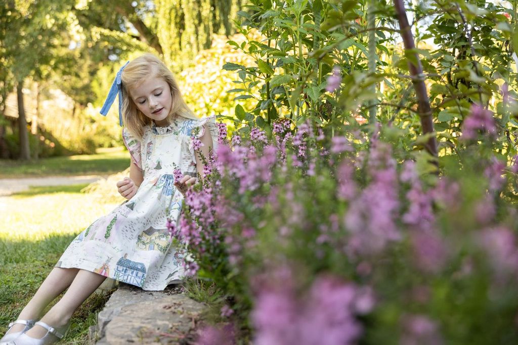 Young girl sitting among pink flowers in a garden