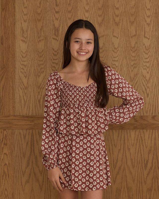 young girl  wearing a patterned dress against a wooden background