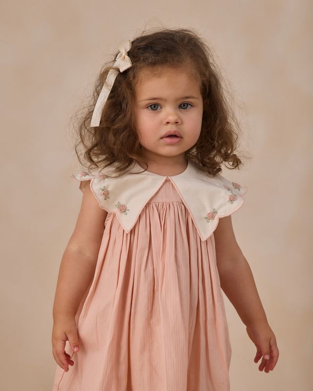 Young girl wearing a pink dress with a white collar against a beige background
