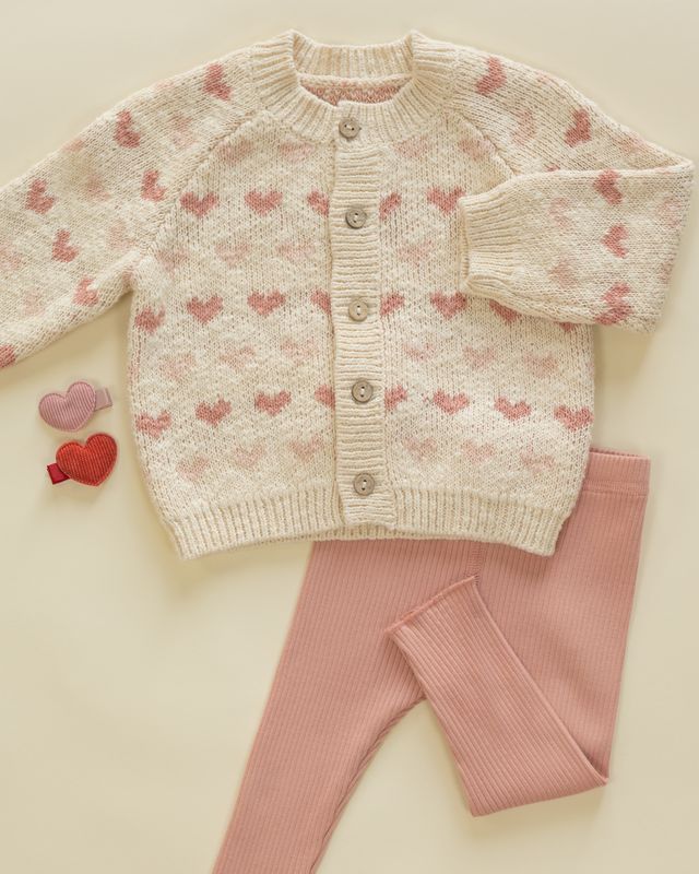 Knitted baby sweater with heart pattern and pink pants on a light background