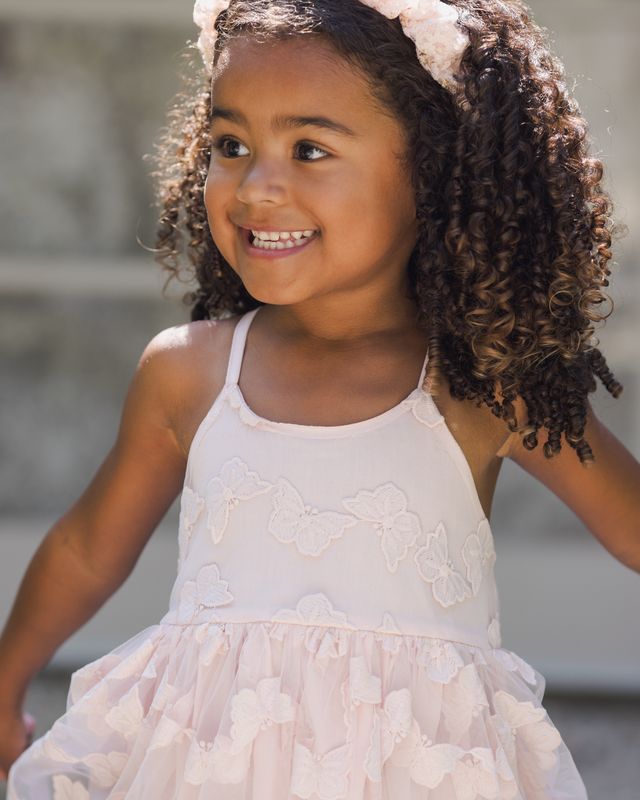 Young girl wearing a light pink dress with butterfly details outdoors.