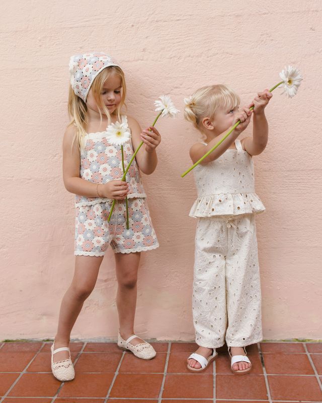 Two young girls holding flowers against a pink wall.
