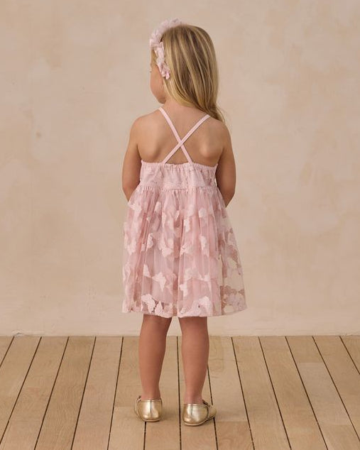 back of a dress with Young girl in a pink butterfly dress standing on a wooden floor with a beige wall background