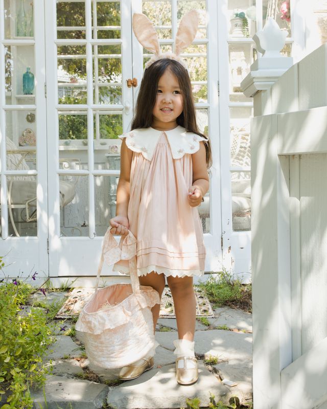 Young girl in a pink dress with bunny ears standing in a garden.