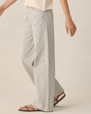 Young Woman wearing a beige top and striped pants on a plain background