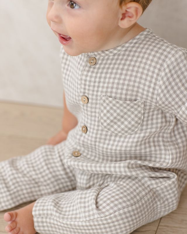 Baby wearing a sage checkered outfit sitting on a wooden floor.